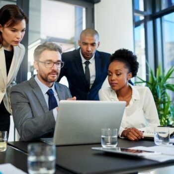 Group of people gather around a laptop to discuss business