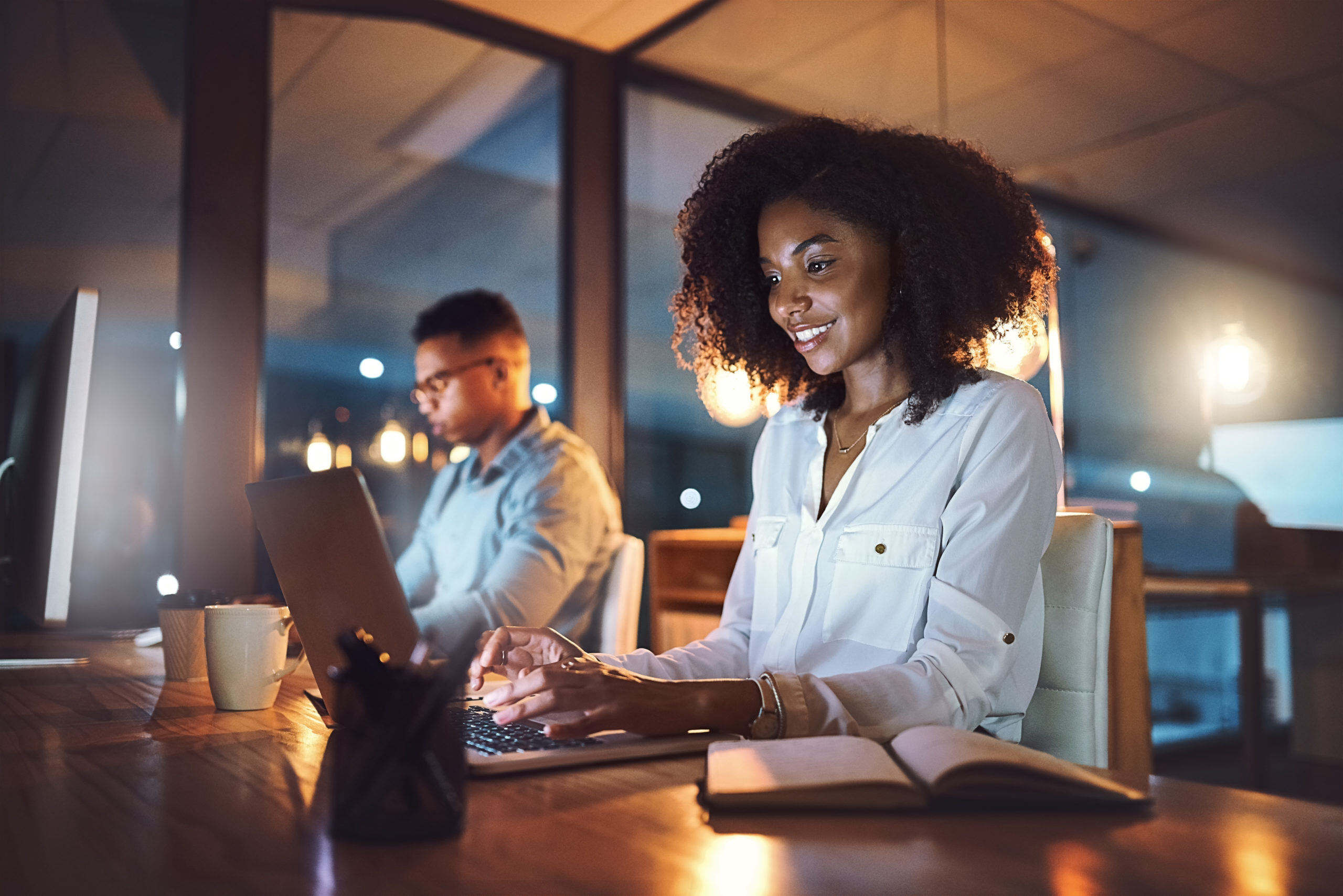 Shot of a young businesswoman working on a laptop alongside her colleague in an office at night