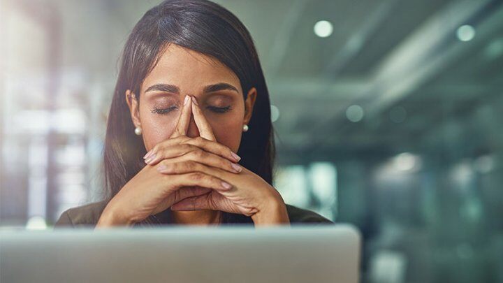 a woman holding her hands together covering her mouth with eyes closed in front of a laptop