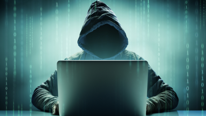 image of a hacker in a black hoodie without a face using a laptop with random binaries arranged vertically