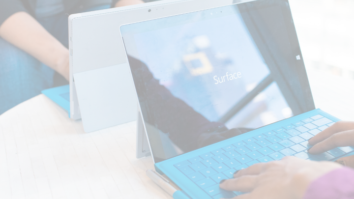 an image of two persons using Microsoft Surface laptops with the screen showing the logo of Microsoft Surface