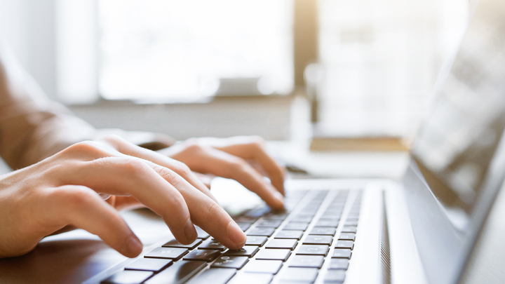 two hands typing on a silver laptop in a bright room