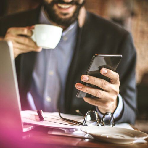 a man watching his phone on his left hand smiling while holding a cup in the other hand