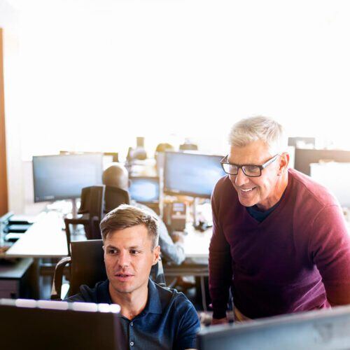 a man in blue collared t-shirt and a man in a maroon sweatshirt looking at a monitor